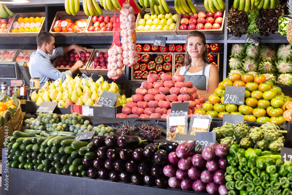 Young girl seller offers fresh ripe fruits and vegetables at the grocery store.