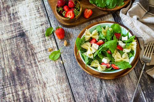 Italian pasta salad with strawberries, arugula, nuts, soft cheese dressed with balsamic sauce on the wooden table. Copy space.
