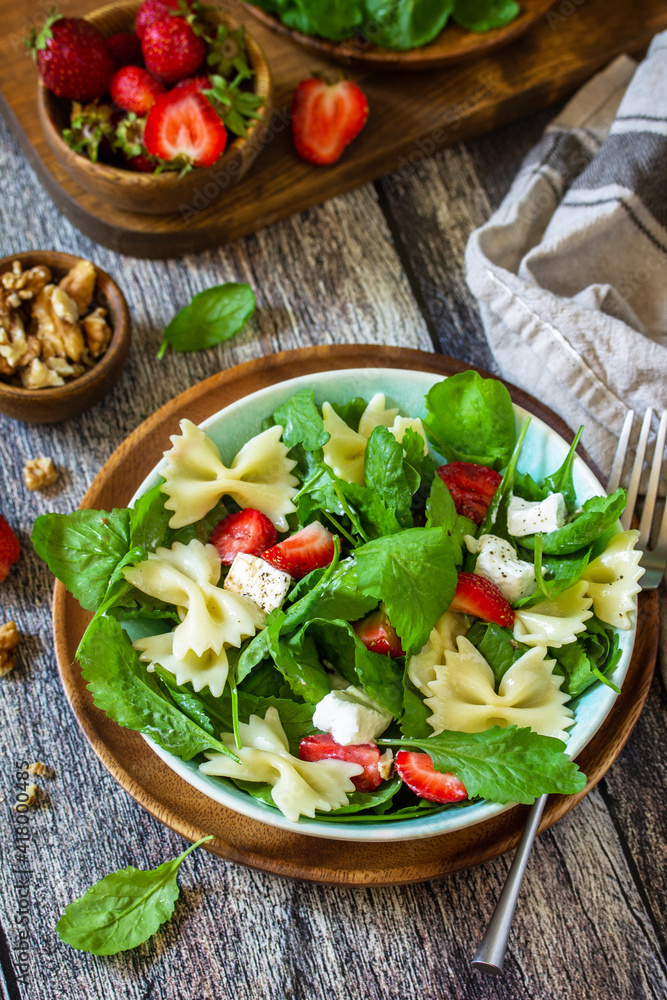 Italian pasta salad with strawberries, arugula, nuts, soft cheese dressed with balsamic sauce on the wooden table. Italian pasta salad with strawberries, arugula, nuts, soft cheese dressed with balsamic sauce on the wooden table.