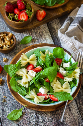 Italian pasta salad with strawberries, arugula, nuts, soft cheese dressed with balsamic sauce on the wooden table.