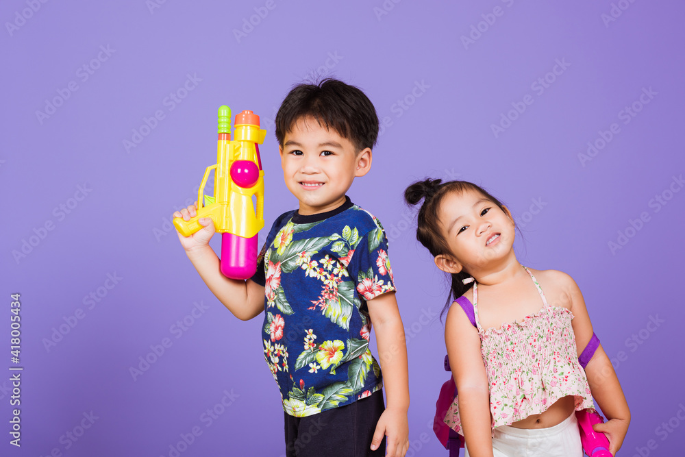 Two Happy Asian little boy and girl holding plastic water gun, Thai children funny hold toy water pistol and smile, studio shot isolated on purple background, Thailand Songkran festival day culture. Two Happy Asian little boy and girl holding plastic water gun, Thai children funny hold toy water pistol and smile, studio shot isolated on purple background, Thailand Songkran festival day culture.