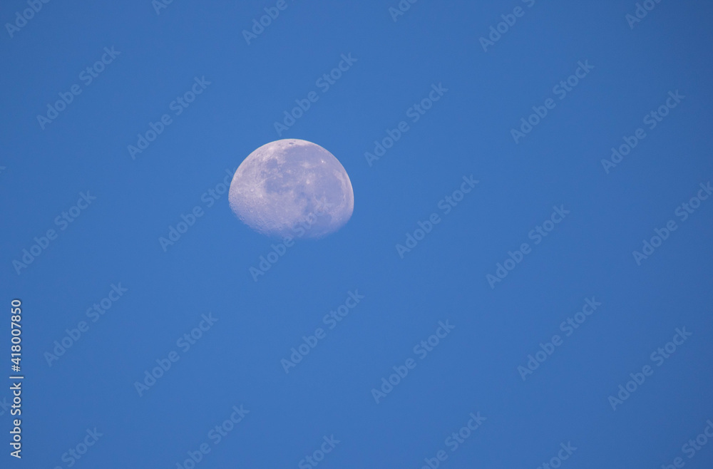 Three quarter moon isolated hanging in a blue daylight sky image for background use
