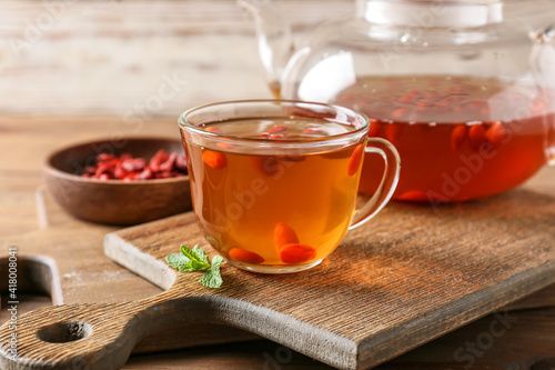 Teapot and glass cup of hot tea with goji berries on wooden background