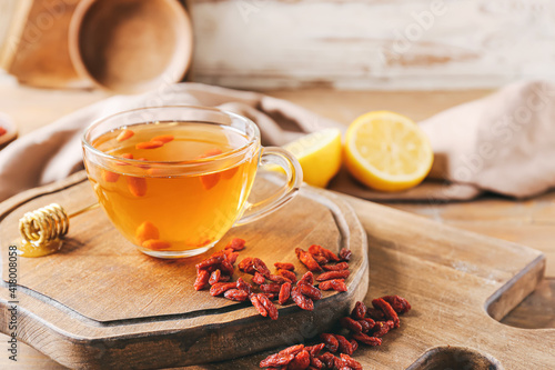 Fotografie Glass cup of hot tea with goji berries on light wooden background
