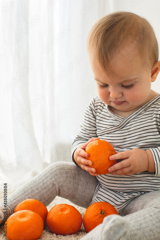 Cute baby girl are sitting with mandarin white background interior. Funny child explores the fruit Cute baby girl are sitting with mandarin white background interior. Funny child explores the fruit