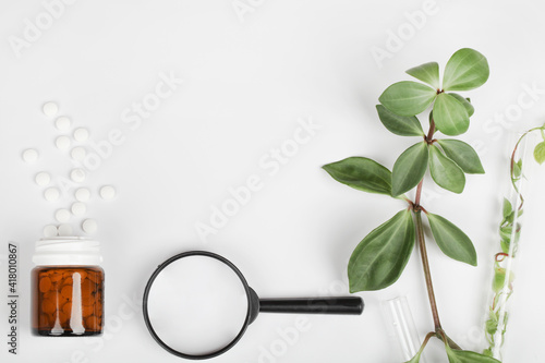 Herbal pills in glass bottle,magnifying glass and green plant leaves on white background.alternative medicine and healthy lifestyle concept.copy space photo