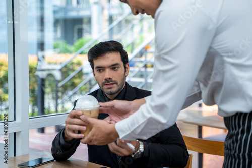 Professional Barista serving coffee and communicating with businessman in coffee shop.