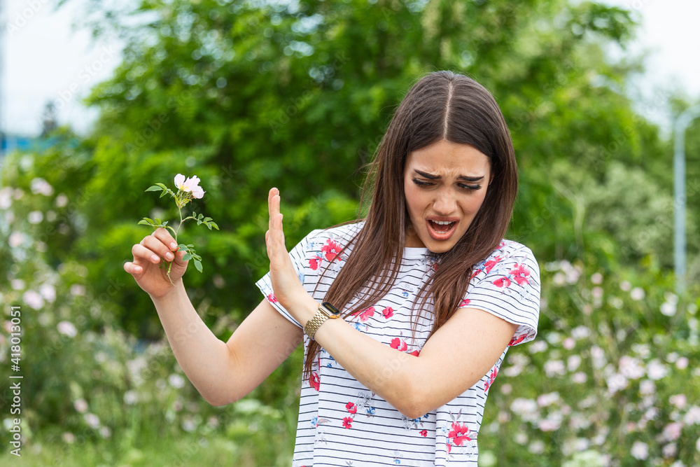 Young woman with Pollen allergy holding a flower and saying no.. Young woman with pollen and grass allergies. Flowering trees in background. Spring Seasonal allergies and health problems. Young woman with Pollen allergy holding a flower and saying no.. Young woman with pollen and grass allergies. Flowering trees in background. Spring Seasonal allergies and health problems.