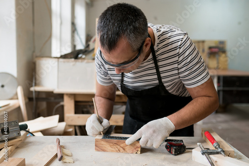 Man carpenter measuring a wooden board with a ruler with scale in workshop. Joinery work on the production and renovation of wooden furniture. Small Business Concept