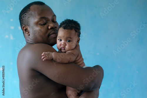 African father holds his baby girl on blue background, 4 mouth baby, man is not wearing a shirt