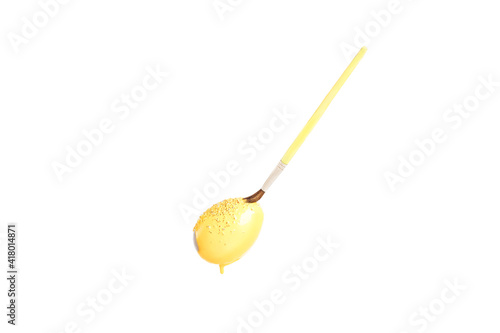 On flying white egg, bright yellow paint sprinkled with sparkles against white background sticks, brush touched tip of egg. Preparing for the religious holiday Easter, painting eggs for the event