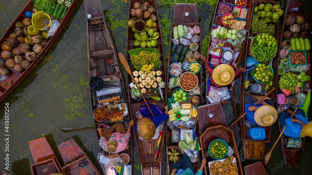 Fototapeta premium Aerial view famous floating market in Thailand, Damnoen Saduak floating market, Farmer go to sell organic products, fruits, vegetables and Thai cuisine, Tourists visiting by boat, Ratchaburi, Thailand