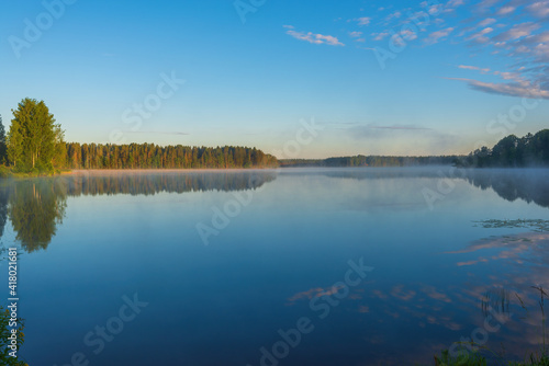 Morning steam over the Roshchinsky lake, clear sky and mirror-like surface of the water. Holy Trinity Alexander Svirsky Monastery in the Leningrad region, known for architectural monuments.