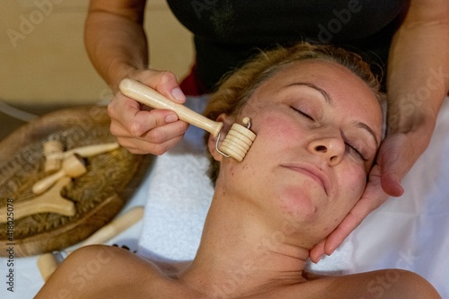 Masseuse giving a facial massage to a client with wood therapy