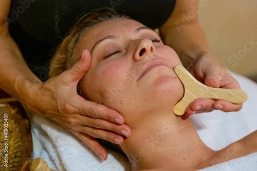 Masseuse giving a facial massage to a client with wood therapy