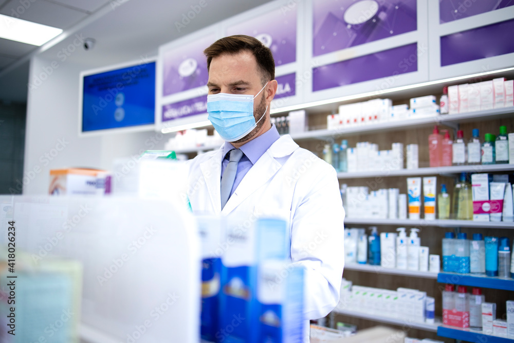 Pharmacist wearing face mask and white coat working in drug store during corona virus pandemic. Healthcare and medicine. Pharmacist wearing face mask and white coat working in drug store during corona virus pandemic. Healthcare and medicine.