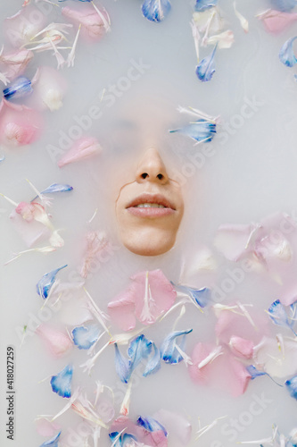 A sensual portrait of a woman in a bath with milk and flowers. Spa treatments, soft skin and soft pastel shades.