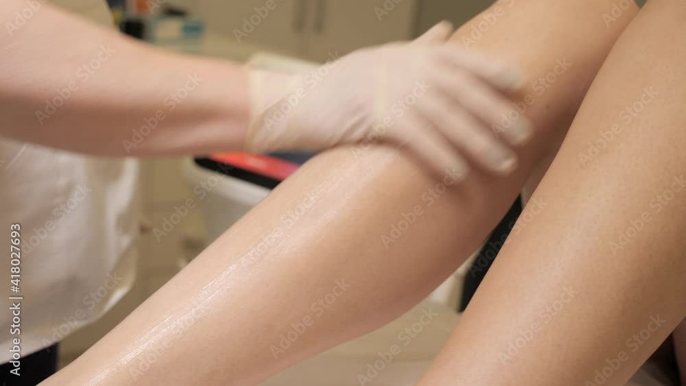 Caring hands of female dermatologist cosmetologist doctor applying epilation gel cream on smooth healthy skin of woman legs before procedure depilation waxing. Beauty and spa service concept. Caring hands of female dermatologist cosmetologist doctor applying epilation gel cream on smooth healthy skin of woman legs before procedure depilation waxing. Beauty and spa service concept.