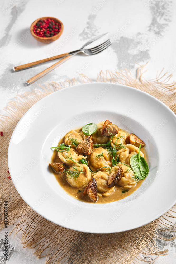 Dumplings Food Restaurant Plate. Dumplings With Creamy Porcini Sauce. White restaurant plate on white table. Rustic restaurant food concept. Dumplings Food Restaurant Plate. Dumplings With Creamy Porcini Sauce. White restaurant plate on white table. Rustic restaurant food concept.