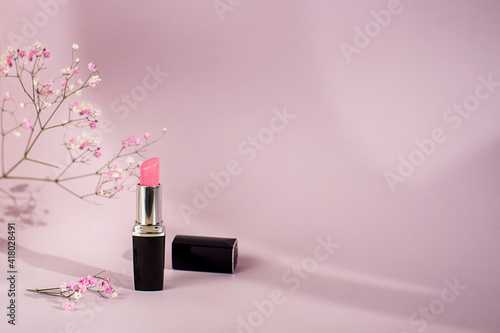 Single tube of pink lipstick on pink background with flowers