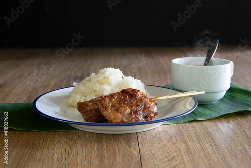 Grilled Pork and Sticky rice in white dish with hot coffee in cup on banana leaf and brown wooden table photo