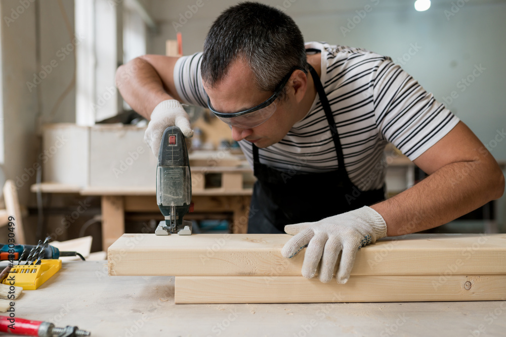 Carpenter working on wood with electric jigsaw in workshop. Joinery work on the production and renovation of wooden furniture. Small Business Concept Carpenter working on wood with electric jigsaw in workshop. Joinery work on the production and renovation of wooden furniture. Small Business Concept