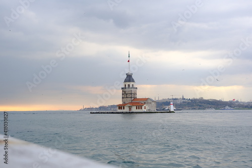 The Maiden's Tower under gray cloudy sky, Bosphorus, Istanbul, Turkey during overcast weather with sunshine reflection in bosporus sea.  Groups of seagulls flying on sea. İstanbul Turkey 01.03.2021 © SKahraman