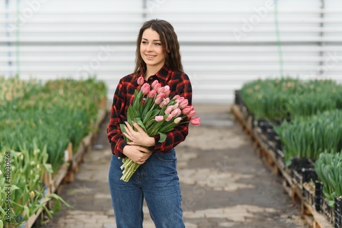 Young beautiful woman greenhouse worker holds a blooming tulips in her hands and smiles.