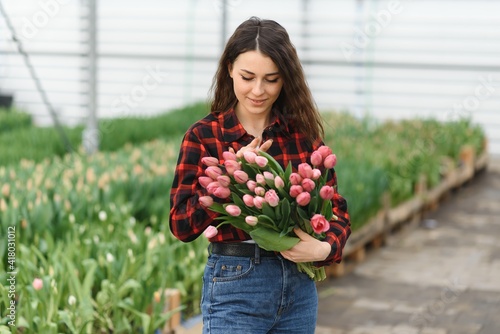 Beautiful young smiling girl, worker with flowers in greenhouse. Concept work in the greenhouse, flowers.