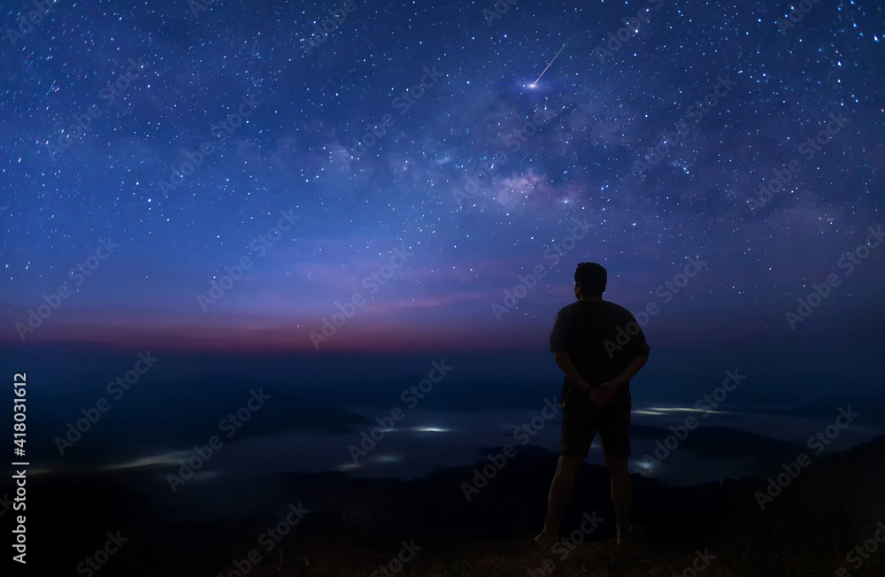 Colorful night sky with stars and silhouette of a standing man on the stone. Blue milky way with man on the mountain. High Rocks. Background with galaxy and silhouette of a man. Colorful night sky with stars and silhouette of a standing man on the stone. Blue milky way with man on the mountain. High Rocks. Background with galaxy and silhouette of a man.