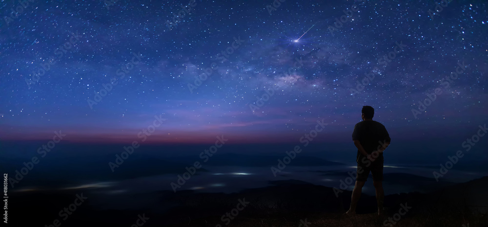 Colorful night sky with stars and silhouette of a standing man on the stone. Blue milky way with man on the mountain. High Rocks. Background with galaxy and silhouette of a man. Colorful night sky with stars and silhouette of a standing man on the stone. Blue milky way with man on the mountain. High Rocks. Background with galaxy and silhouette of a man.