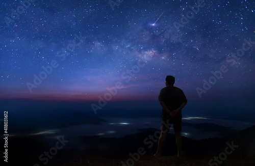 Colorful night sky with stars and silhouette of a standing man on the stone. Blue milky way with man on the mountain. High Rocks. Background with galaxy and silhouette of a man. 