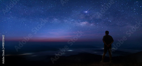Colorful night sky with stars and silhouette of a standing man on the stone. Blue milky way with man on the mountain. High Rocks. Background with galaxy and silhouette of a man. 