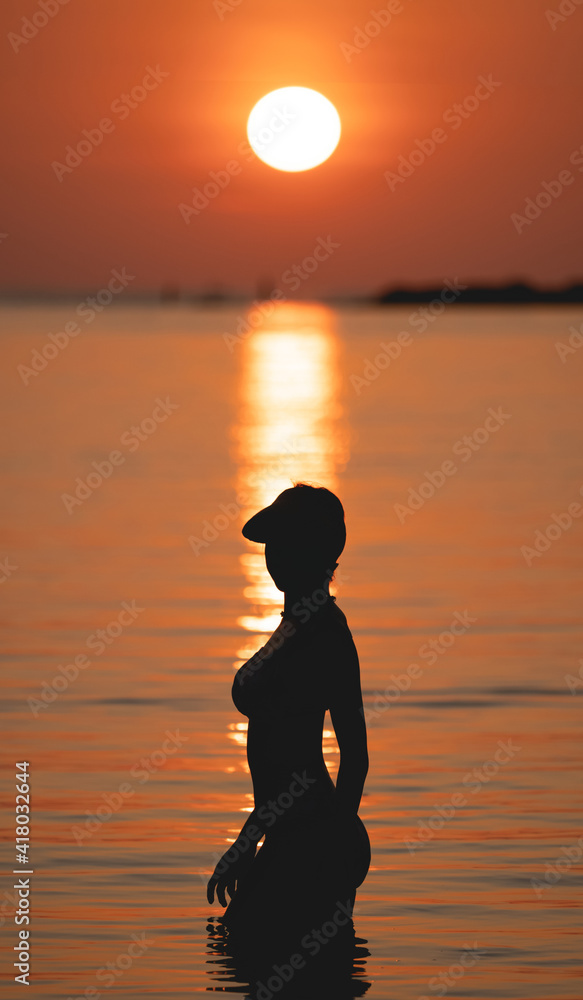Sunset ocean view. Sun above the sea on orange sky. Woman standing on beach.