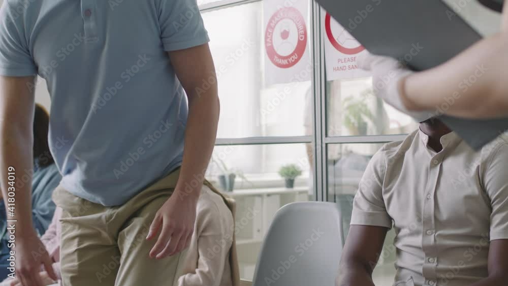 Low-angle waist-up shot with slowmo of caucasian man wearing protective mask in multiethnic hospital queue standing up following doctor going to get vaccinated Low-angle waist-up shot with slowmo of caucasian man wearing protective mask in multiethnic hospital queue standing up following doctor going to get vaccinated