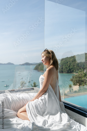 Sexy woman sitting near the window at villa with ocean view.