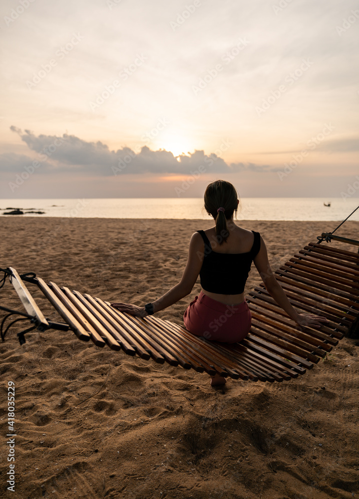 Silhouette of a woman sitting on a swing or cradle on the beach at sunset.