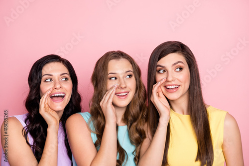 Photo of impressed nice long hairdo three ladies tell secret look empty space wear pastel cloth isolated on pink color background