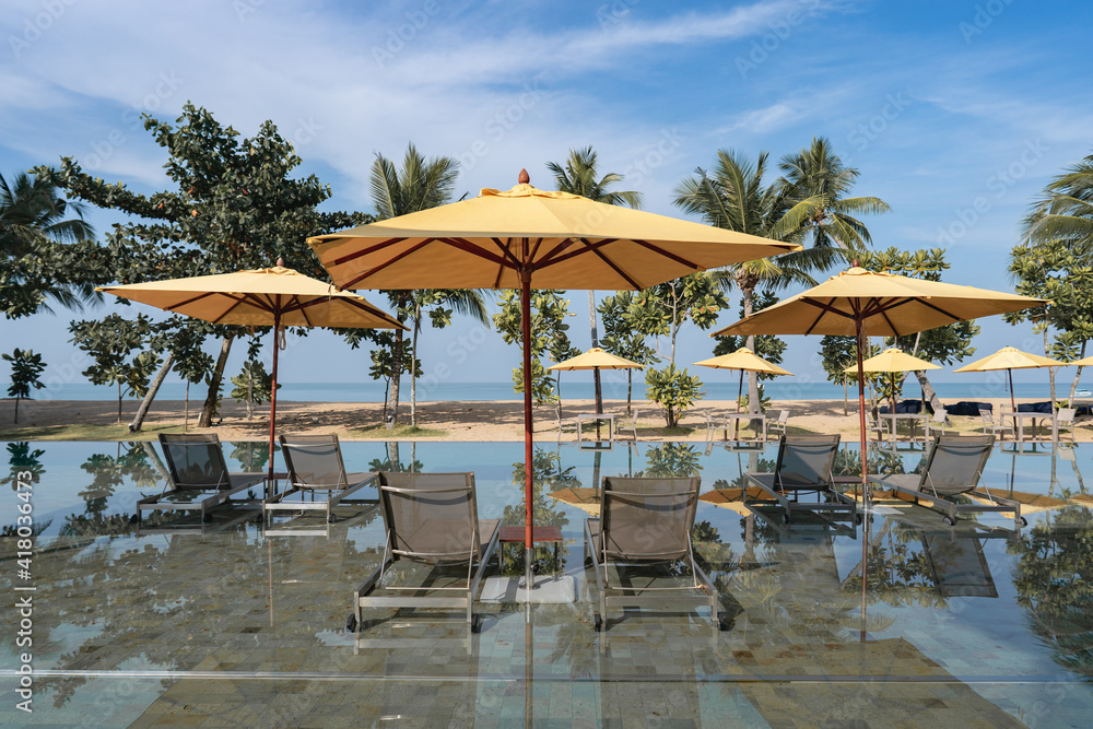 Deckchairs with yellow umbrella in tropical resort hotel pool near beach.