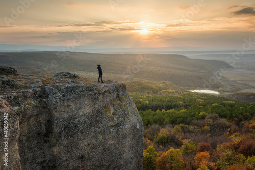 Silhouette of a woman on the top of a rock enjoys the view of sunset over an autumn forest