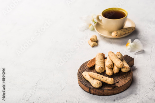 Long shortbread cookies on a dark wooden board with a cup of tea on a light background. Side view with a copy space for the text.