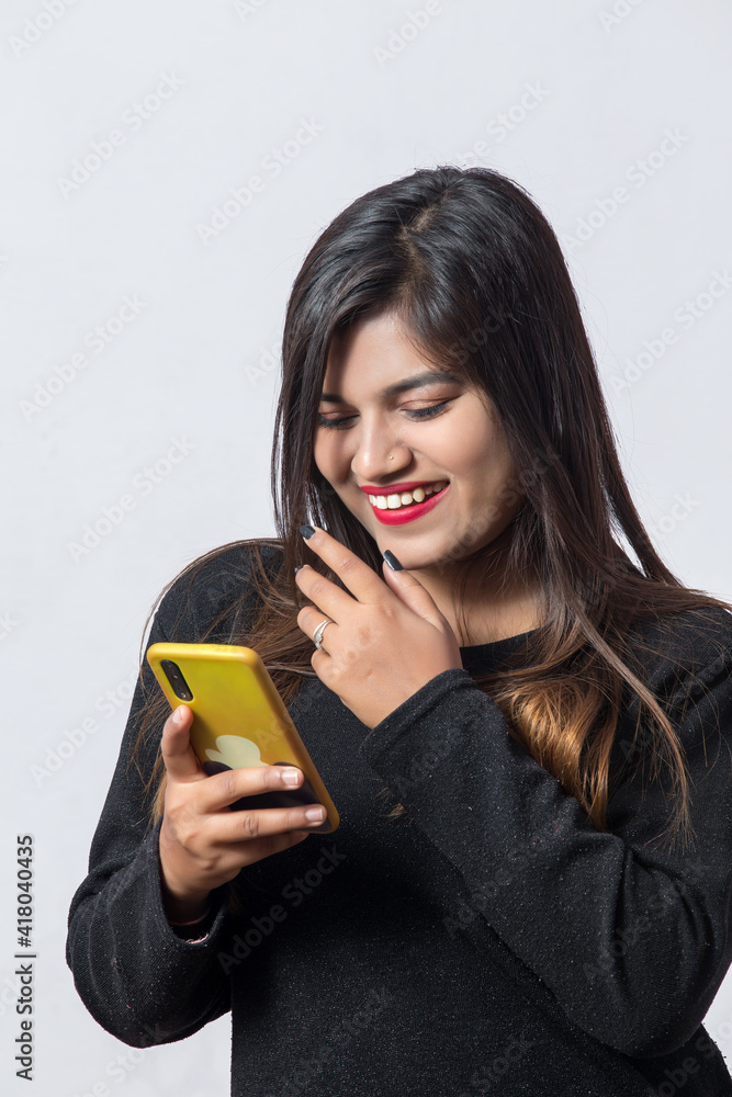 Indian girl posing wit a laughing expression while checking her mobile for modeling photo shoot in studio against white background Indian girl posing wit a laughing expression while checking her mobile for modeling photo shoot in studio against white background