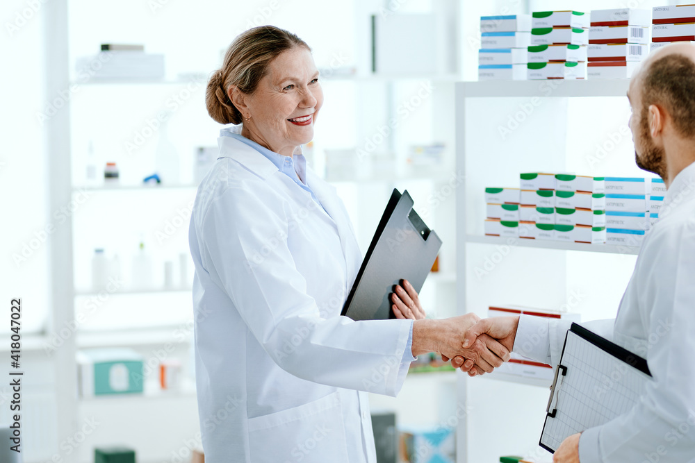 friendly female pharmacist shaking hands with a new employee. friendly female pharmacist shaking hands with a new employee.