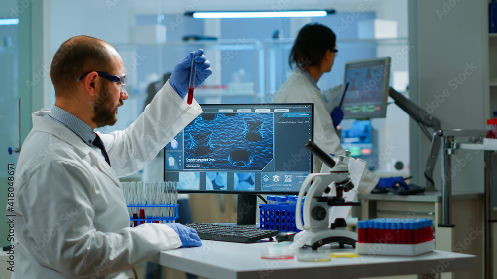 Fototapeta premium Scientist man examining blood samples and liquid working in modern equipped laboratory. Team of doctors analysing vaccine evolution using high tech researching diagnosis against covid19