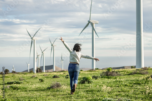 Unrecognizable woman running in meadow with windmills