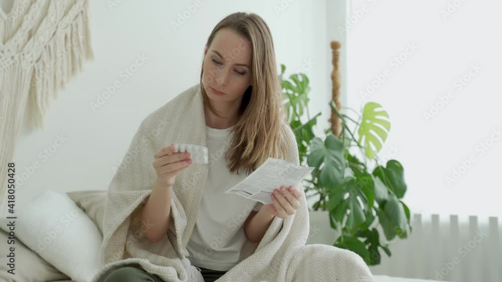 A woman reads the medical instructions before taking the pills sitting on the bed in her bedroom A woman reads the medical instructions before taking the pills sitting on the bed in her bedroom