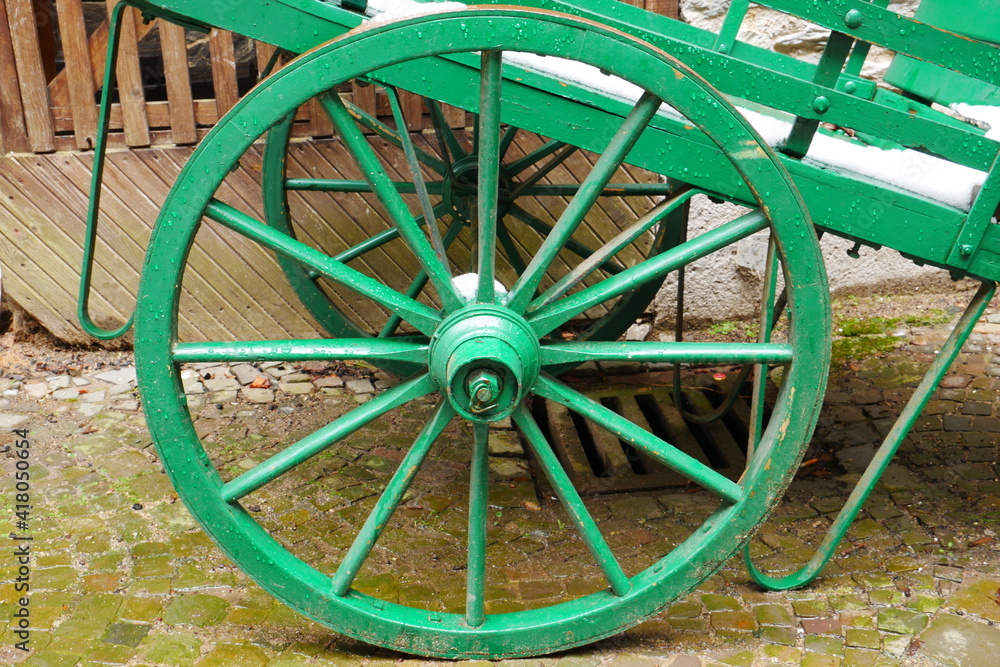 green old wagon wheel of a medieval handcart with snow on the cart