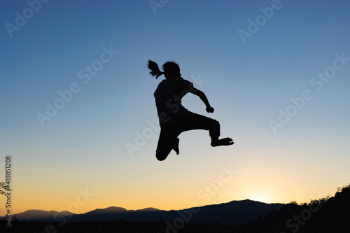 Silhouette of happy child jumping playing on mountain at sunset or sunrise