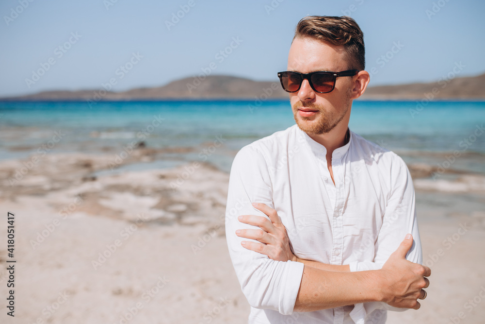 portrait of a young man in sunglasses and a white shirt against the background of the sea and rocks. Sumer holidays 