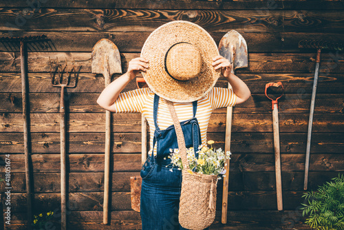 Woman wearing straw hat and blue denim dungarees relaxing near wooden old summerhouse wall on sunny day. photo